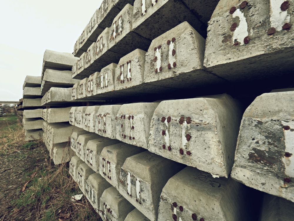 Sleepers stock in railway depot. New concrete railway ties stored for reconstruction of old railway station. Old houses in background